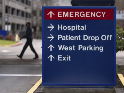 A hospital directional sign reads "EMERGENCY," "Hospital," "Patient Drop Off," "West Parking," and "Exit."