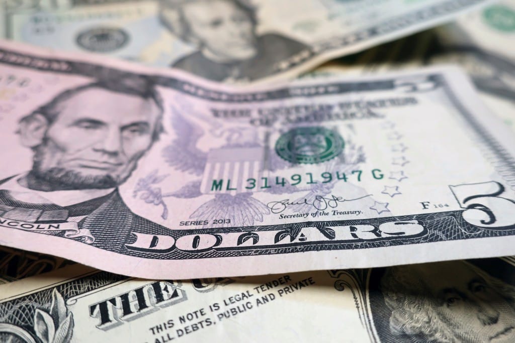 A close-up, shallow-focus shot of a U.S. five-dollar bill featuring Abraham Lincoln, layered on top of other various denominations of U.S. currency.