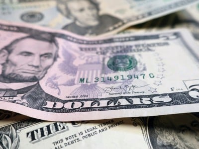A close-up, shallow-focus shot of a U.S. five-dollar bill featuring Abraham Lincoln, layered on top of other various denominations of U.S. currency.