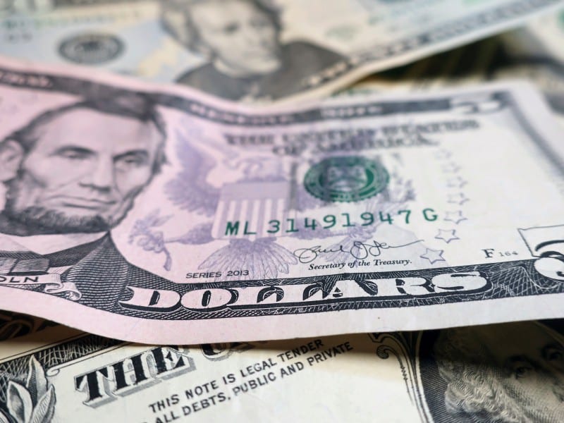 A close-up, shallow-focus shot of a U.S. five-dollar bill featuring Abraham Lincoln, layered on top of other various denominations of U.S. currency.