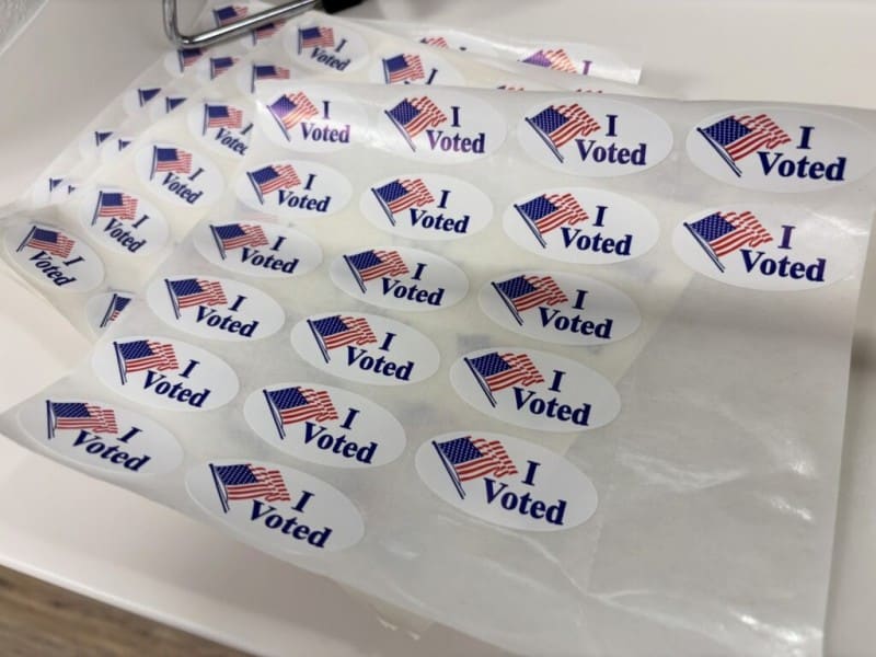 Sheets of white oval stickers feature a waving American flag graphic next to the dark blue text "I Voted."