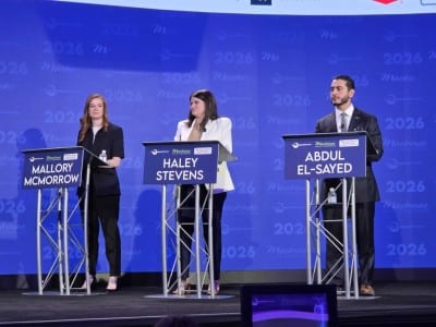 Mallory McMorrow, Haley Stevens, and Abdul El-Sayed stand behind individual metal lecterns with blue nameplates on a stage. The bright blue backdrop features repeating text and logos for the "2026 Mackinac Policy Conference."