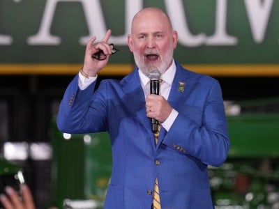 U.S. Rep. Derrick Van Orden, a bald man with a white beard speaks into a microphone while wearing a bright blue suit jacket and a yellow-and-blue striped tie.