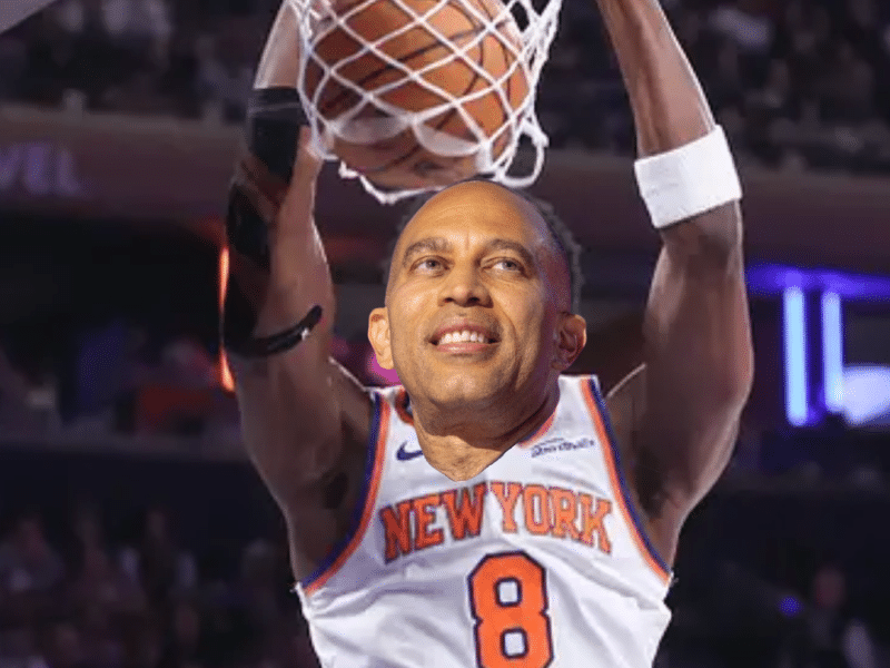 **Alt Text:** A photoshopped image showing the head of politician Hakeem Jeffries superimposed onto the body of a basketball player executing a slam dunk. The player wears a white New York Knicks jersey with the number 8, hanging from the rim as the basketball passes through the net. The background shows a blurred stadium crowd under arena lighting.