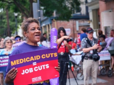 A demonstrator holds a sign reading "MEDICAID CUTS = JOB CUTS" at a rally.