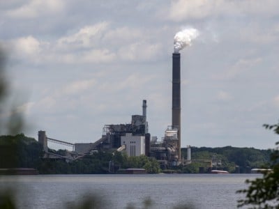 Industrial power plant on a wooded shoreline in in Warrick County, Indiana with white smoke billowing from a tall smokestack