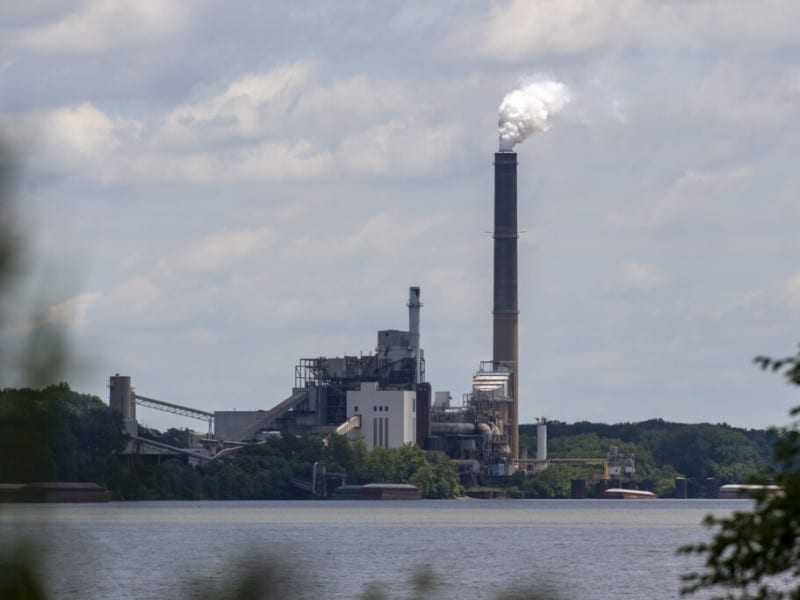 Industrial power plant on a wooded shoreline in in Warrick County, Indiana with white smoke billowing from a tall smokestack
