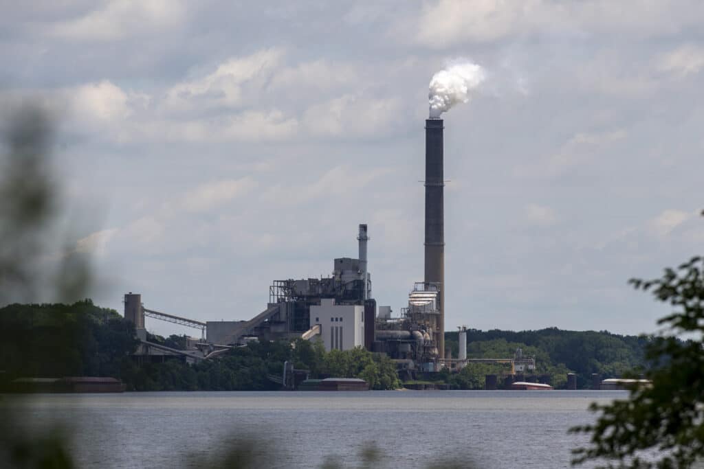Industrial power plant on a wooded shoreline in in Warrick County, Indiana with white smoke billowing from a tall smokestack