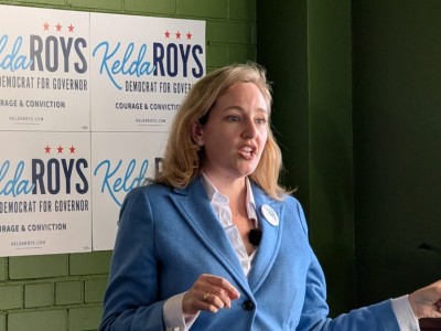 Kelda Roys speaks in front of campaign signs reading "Kelda Roys Democrat for Governor Courage & Conviction."