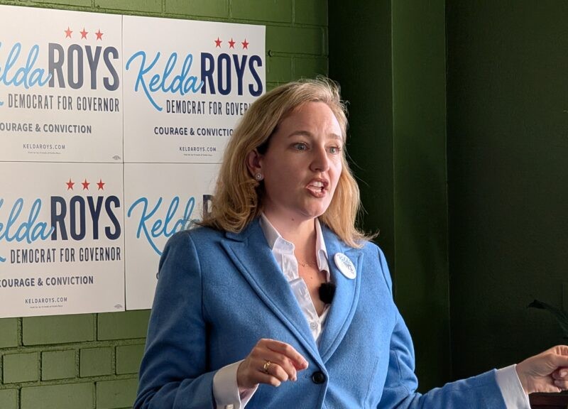 Kelda Roys speaks in front of campaign signs reading "Kelda Roys Democrat for Governor Courage & Conviction."