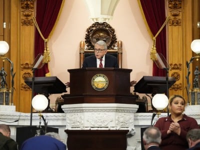 Ohio Governor Mike DeWine speaks at a podium with the Great Seal of Ohio; a sign language interpreter is in the foreground.