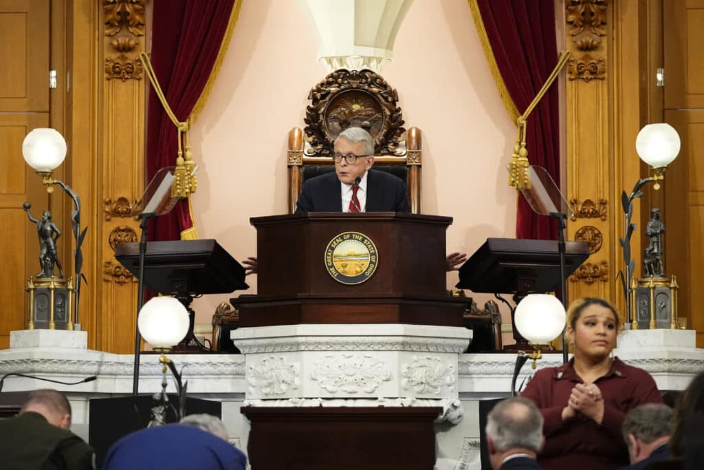 Ohio Governor Mike DeWine speaks at a podium with the Great Seal of Ohio; a sign language interpreter is in the foreground.