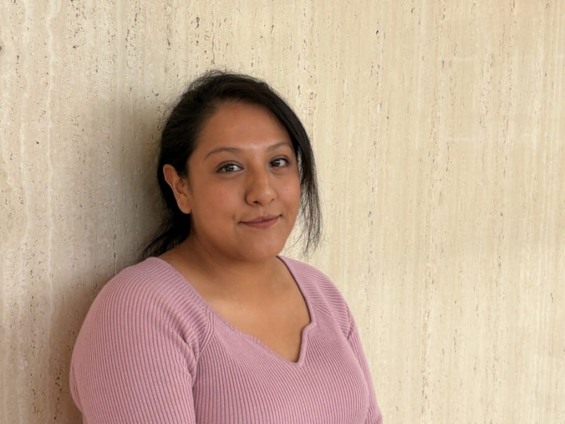 A portrait of Mariana Villegas smiling slightly while leaning against a textured wall.