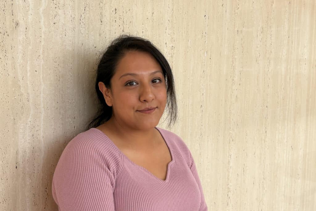 A woman sits against a reflective stone wall in a courthouse.