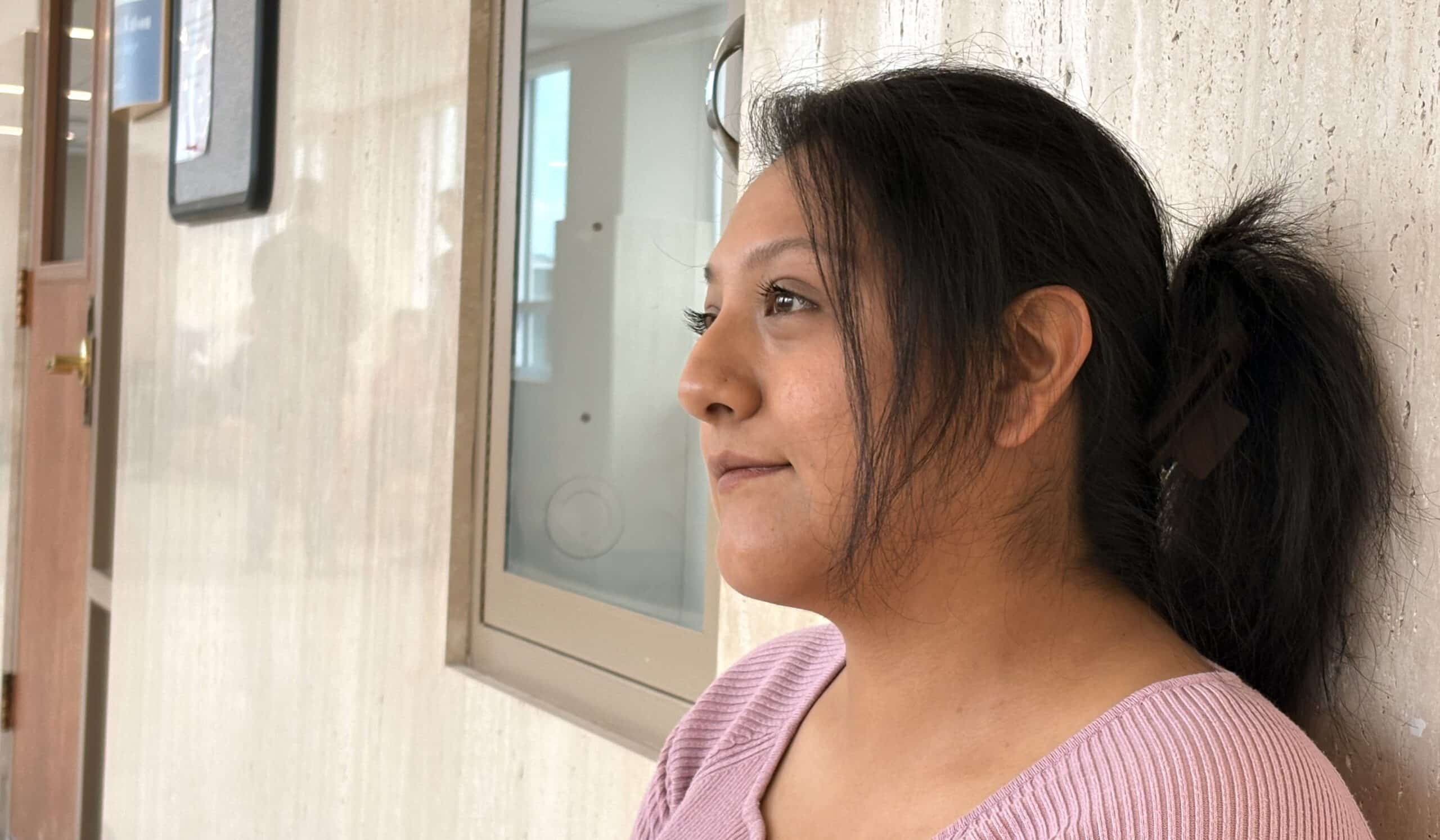A 27-year-old woman sits against a reflective courthouse wall