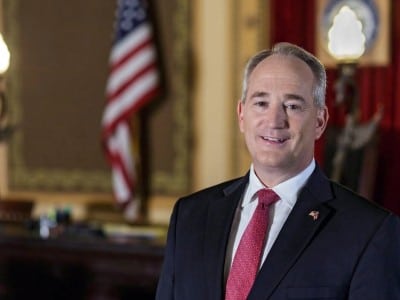 Official portrait of Ohio Auditor Keith Faber in a suit and tie, with an American flag blurred in the background.