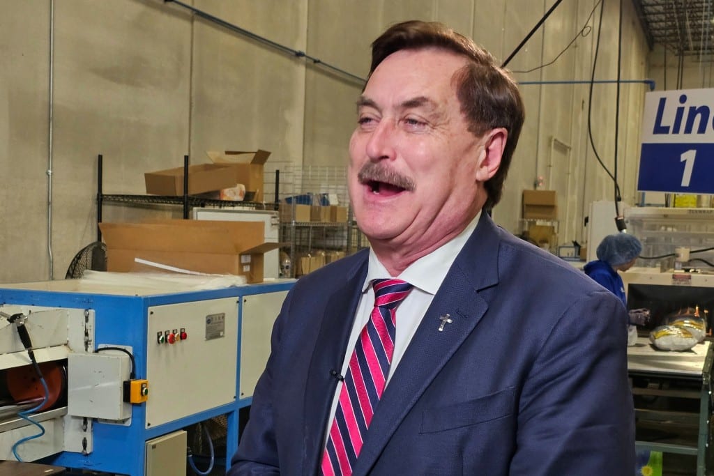 Mike Lindell speaks inside a manufacturing facility with machinery in the background.