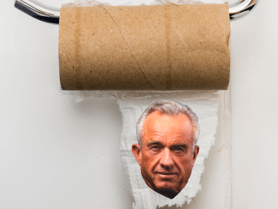 An empty, brown cardboard toilet paper roll on a chrome holder with a small piece of paper featuring Robert F. Kennedy Jr.'s face.