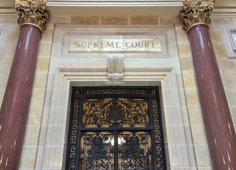 Ornate metal doors of the Wisconsin Supreme Court, flanked by marble columns under an engraved "SUPREME COURT" sign.