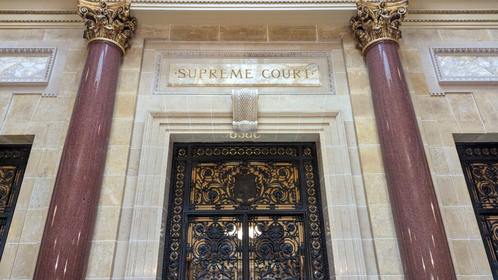 Ornate metal doors of the Wisconsin Supreme Court, flanked by marble columns under an engraved "SUPREME COURT" sign.