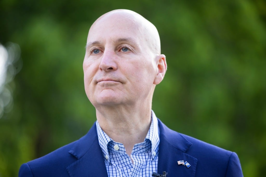 U.S. Sen. Pete Ricketts looks off-camera outdoors against a blurred green background.