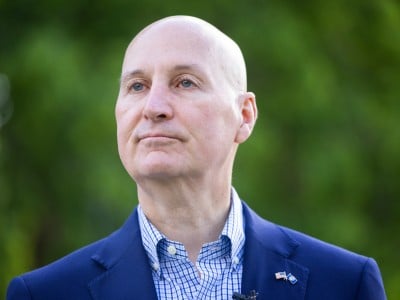 U.S. Sen. Pete Ricketts looks off-camera outdoors against a blurred green background.