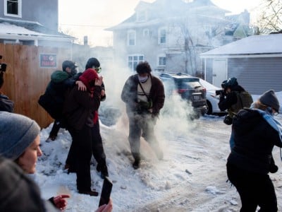 Demonstrators in a snowy alley cover their faces and scatter through thick tear gas smoke
