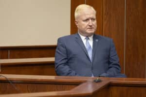 Deputy Secretary of State Wayne Bena sits at the witness stand in a courtroom.