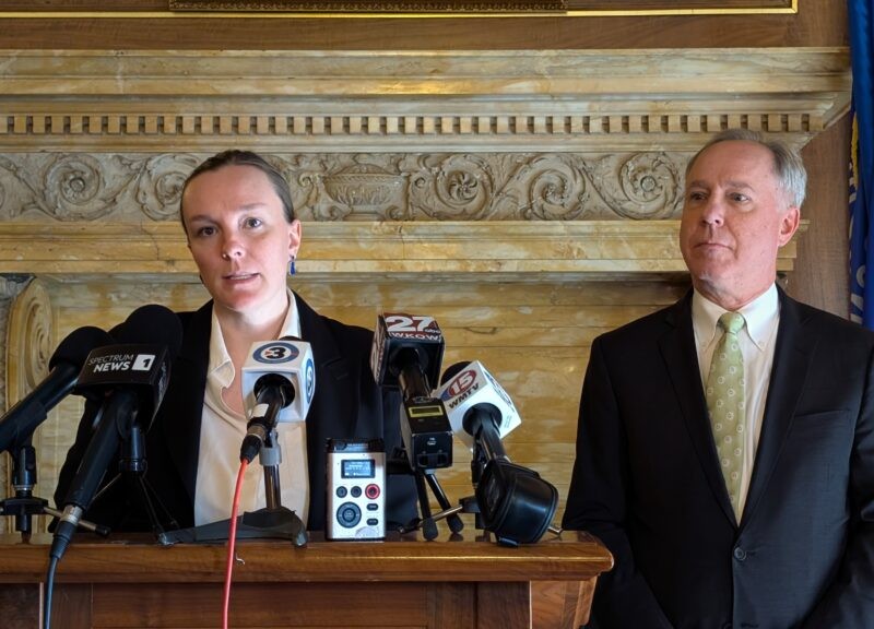 Greta Neubauer speaks into several microphones at a podium while Robin Vos stands beside her.