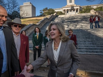 U.S. Sen. Marsha Blackburn smiles and shakes hands on the steps of a grand stone building with a crowd behind her.
