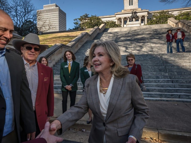 U.S. Sen. Marsha Blackburn smiles and shakes hands on the steps of a grand stone building with a crowd behind her.