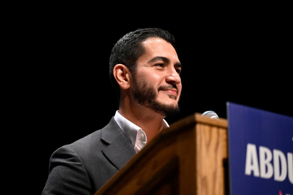 U.S. Senate candidate Abdul El-Sayed smiles while standing at a podium with a microphone.