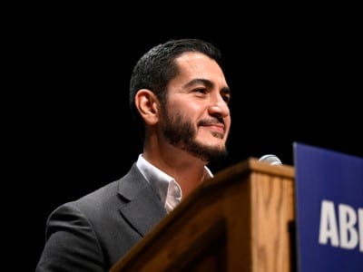 U.S. Senate candidate Abdul El-Sayed smiles while standing at a podium with a microphone.