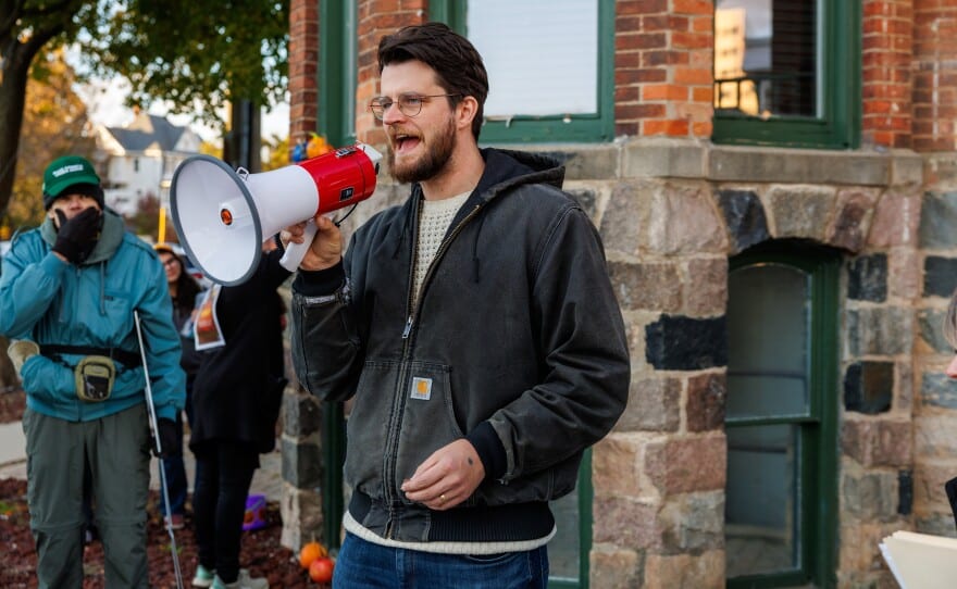William Lawrence speaks into a megaphone outdoors in front of a brick building.