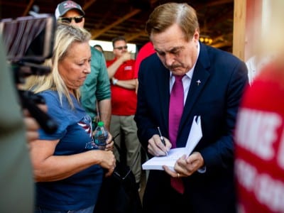 Mike Lindell signs a book for a woman standing next to him in a crowd.