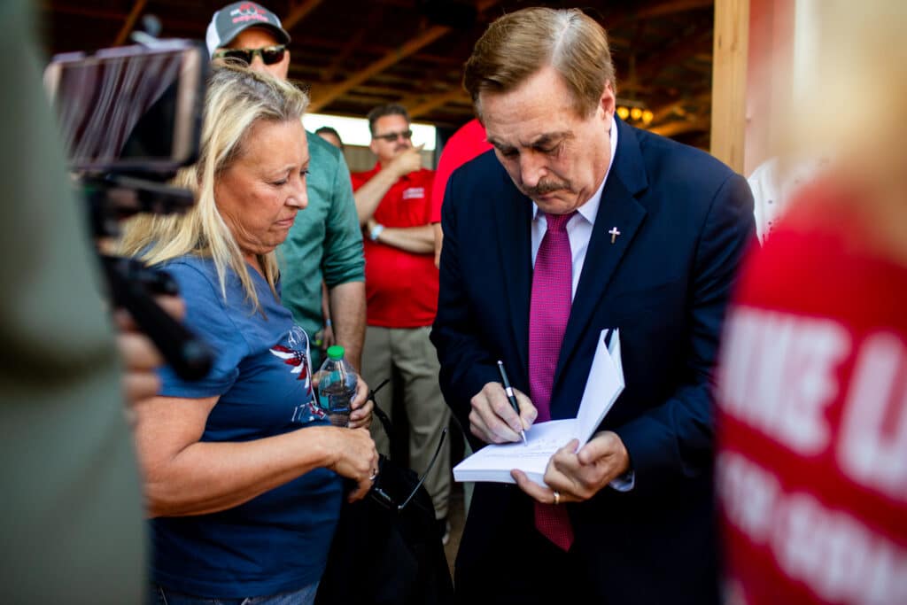 Mike Lindell signs a book for a woman standing next to him in a crowd.
