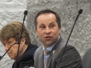 Sen. Spencer Deery speaks into a desk microphone during a committee hearing.