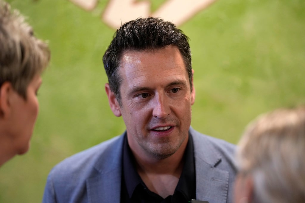 Zach Lahn speaks during a conversation, framed between two people standing near him.