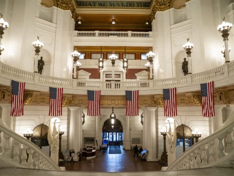 Inside the Capitol building: an ornate marble atrium with grand staircases, hanging American flags and a domed ceiling with gold accents.