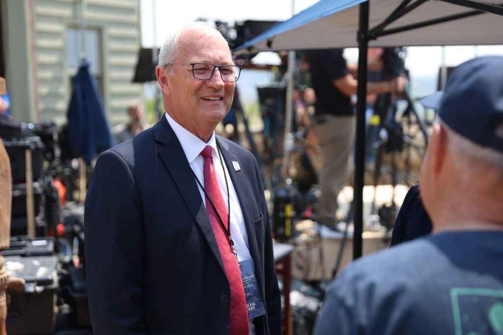 Kevin Cramer smiles in a suit while speaking to a reporter at an outdoor media event.