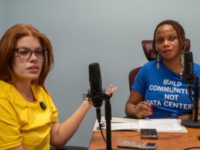 State Reps. Alexis Simmons and Brooklynne Mosley, the latter wearing a shirt reading "BUILD COMMUNITIES NOT DATA CENTERS," speak into studio microphones.