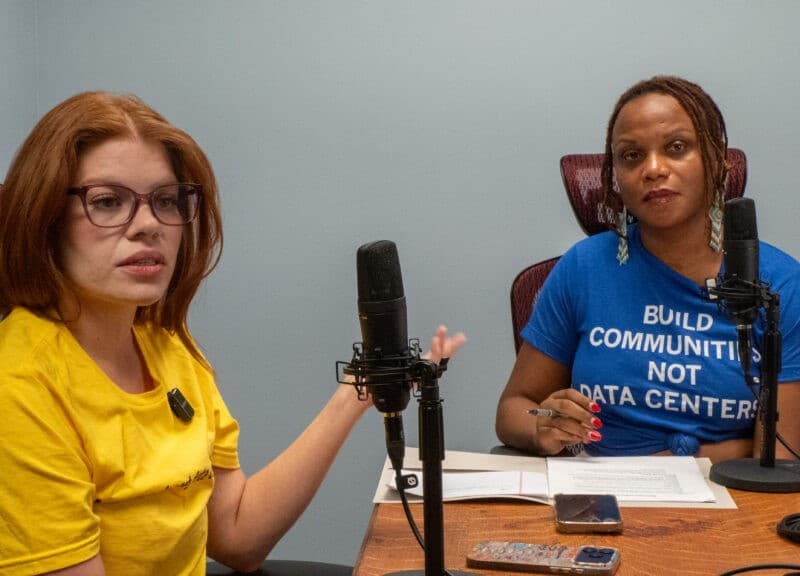 State Reps. Alexis Simmons and Brooklynne Mosley, the latter wearing a shirt reading "BUILD COMMUNITIES NOT DATA CENTERS," speak into studio microphones.