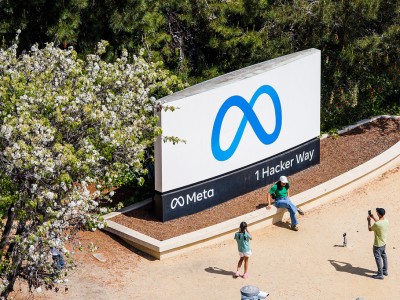 People take photos in front of a large Meta headquarters sign that reads "Meta 1 Hacker Way."