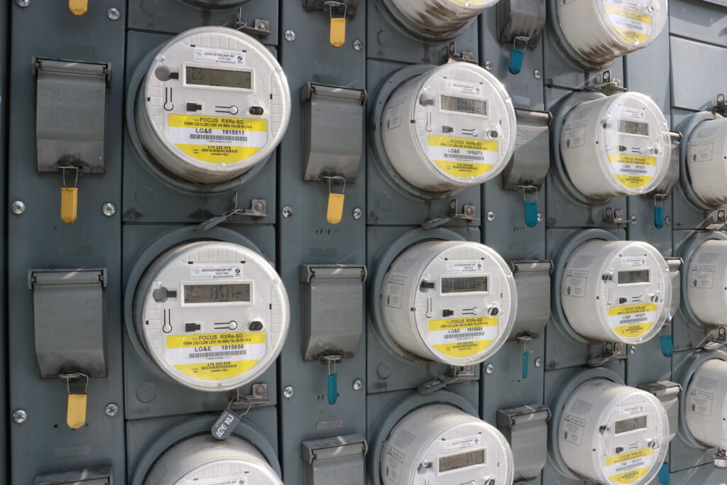 A wall filled with rows of round, digital electric utility meters labeled "LG&E."
