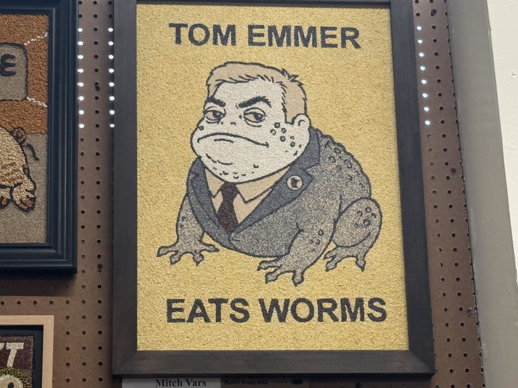 Seed art of a toad wearing a suit jacket depicting the face of Tom Emmer with the text "TOM EMMER EATS WORMS."