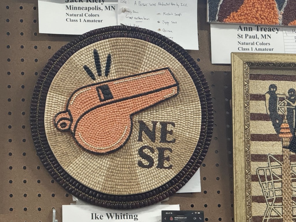 Circular seed art of a whistle blowing, alongside the text "NE SE."