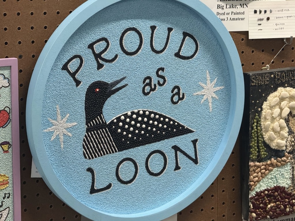 Circular seed art depicting a loon surrounded by stars with text "PROUD as a LOON."