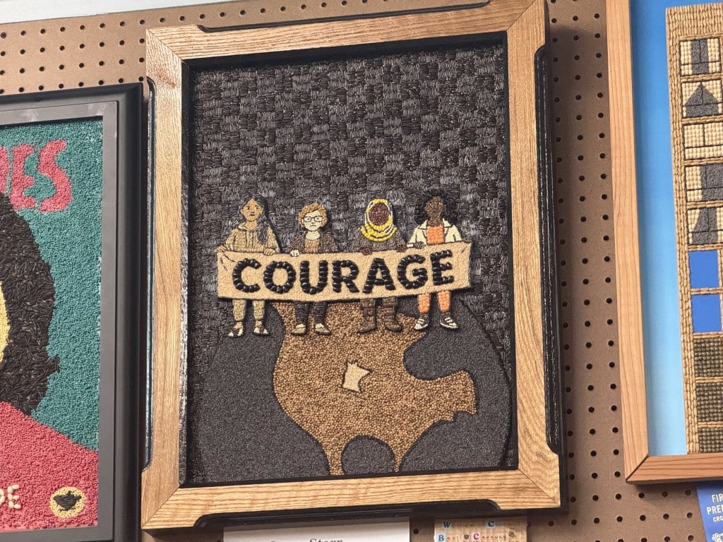 Seed art of four women holding a banner that reads "COURAGE" above a map of Minnesota.
