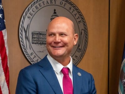 Kansas Secretary of State Scott Schwab smiles in front of the state seal and flags.