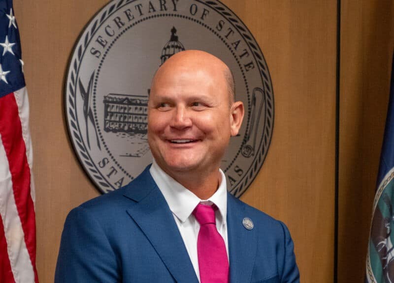 Kansas Secretary of State Scott Schwab smiles in front of the state seal and flags.